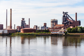 Integrated steelworks on the bank of a river on a partly cloudy summer day - obrazy, fototapety, plakaty