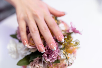 Fototapeta premium Beautiful well-groomed female hands with a beautiful manicure on a bouquet of flowers. Concept of beauty salon manicure, pedicure. Nail care. Cosmetic procedure