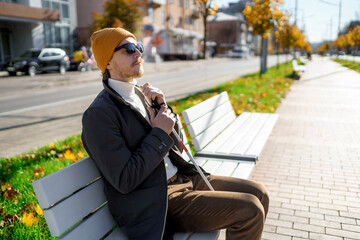 Blind man with a walking stick sitting on a bench in the city