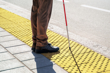 Close-up of a blind man with a walking stick. Stands on a tactile tile for self-orientation while...