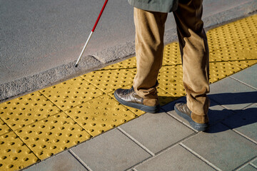 Close-up of a blind man with a walking stick. Stands on a tactile tile for self-orientation while...