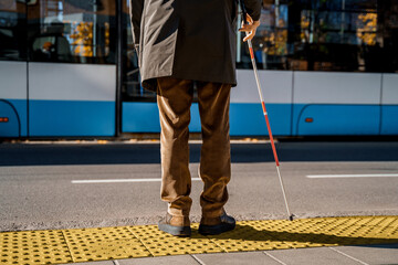 Blind man with a cane stopped on a tactile tile in front of a tram obstacle - obrazy, fototapety, plakaty