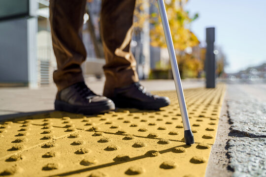 Close-up of a blind man with a walking stick. Stands on a tactile tile for self-orientation while moving through the streets of the city