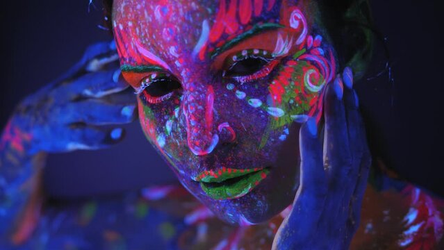 Close-up portrait of girl with a UV pattern on her face, on the eyes and lips bright multi colored makeup. Graceful model posing with UV pattern on body. Body art glowing in ultraviolet light.