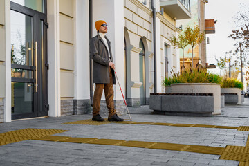 Blind man with a walking stick. Walks on tactile tiles for self-orientation while moving through...