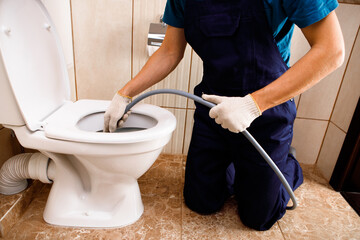 plumber unclogging blocked toilet with hydro jetting at home bathroom