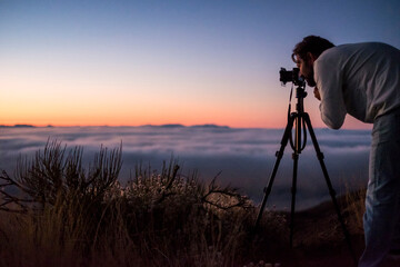 Man photographing with camera against sky during sunset