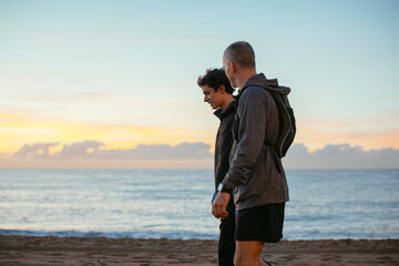 Side view of father and son walking at beach against sky