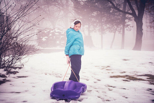 Girl with plastic sled standing on snowy field