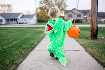 Toddler girl dressed as an alligator carrying Halloween bucket