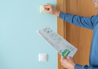 Man with bill lowers temperature on thermostat at home. Concept of energy crisis.