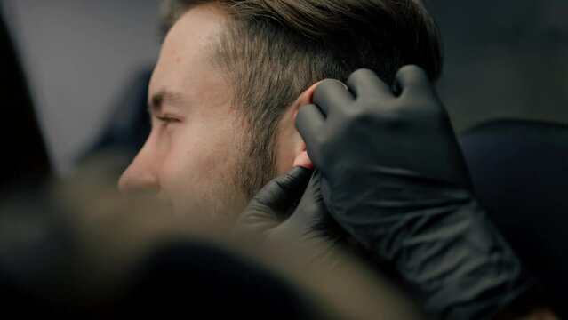 Tattoo piercing studio - a woman makes an ear piercing to a man to a guy