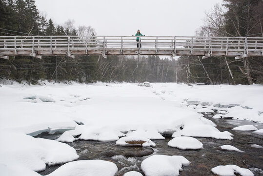 Woman standing on footbridge above frozen river in winter