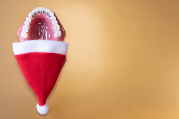 
Lustiger zahnärztlicher Weihnachtshintergrund mit Platzhalter. Zahnmodell mit festsitzender Zahnspange trägt eine Weihnachtsmütze und isst eine Weihnachtskugel - obrazy, fototapety, plakaty