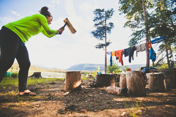 A young woman chops firewood with a small axe while camping at Unna Lake in Bowron Lake Provincial Park.