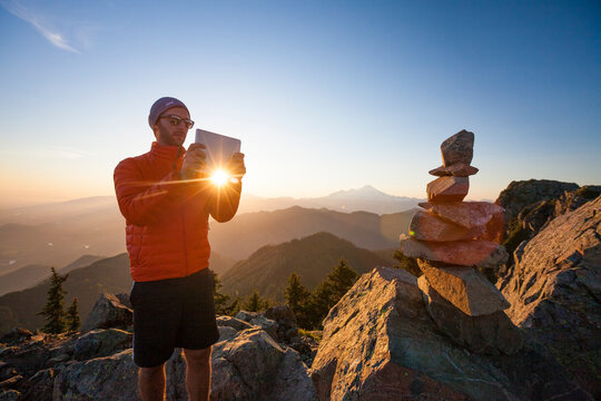 A hiker uses a tablet to take a picture of a cairn on the summit of Sauk Mountain.