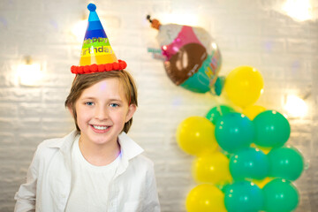 Fototapeta na wymiar happy boy in a birthday hat on the background of balloons at home 