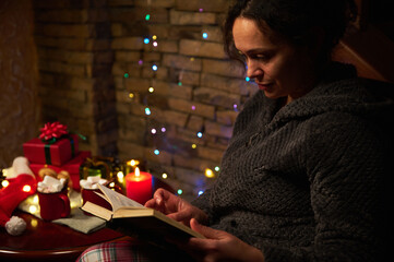 Relaxed pretty woman reading book by candlelight at Christmas holidays