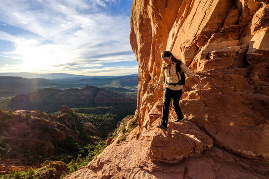 Female hiker walking down rocks at Cathedral Rock with setting sun in background, Arizona, USA
