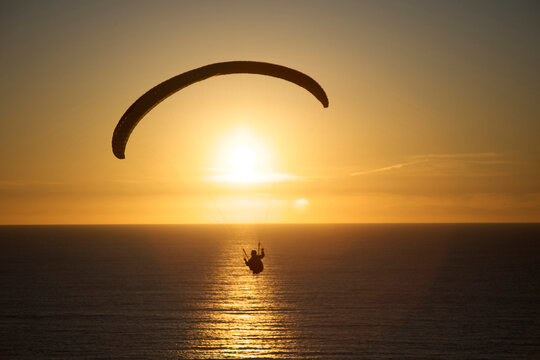 Paraglider rides the wind at sunset over the ocean in California.