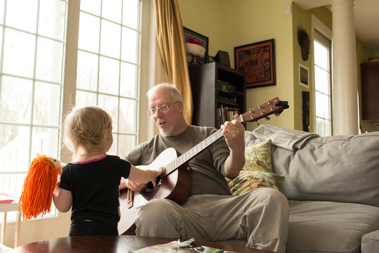 Grandfather Plays Guitar for Young Granddaughter at Home