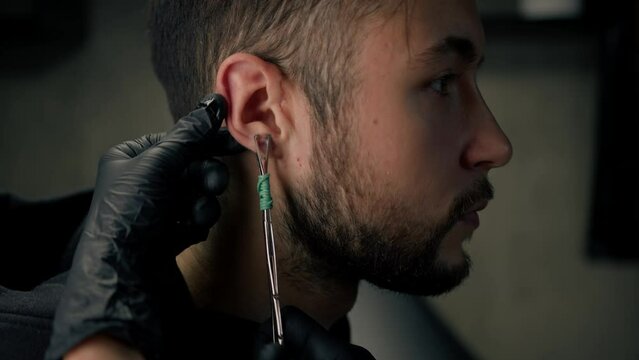 Tattoo piercing studio - a woman makes an ear piercing to a man to a guy