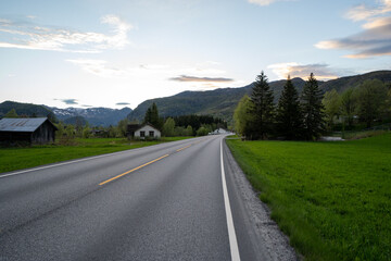 an asphalt road in the norwegian mountains with green grass and trees along the edge