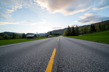 an asphalt road in the norwegian mountains with green grass and trees along the edge and a...