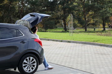 Fototapeta Kobieta siedzi w bagażniku samochodu osobowego, suwa na parkingu w parku. obraz