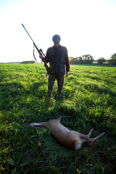 A hunter stands over his kill in a grassy field, during a deer hunting trip in Zealand, Denmark.