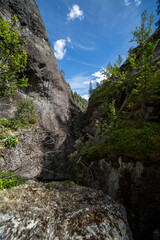 a blue dark narrow valley in Norway Helvete which has a forest with green trees along the edges, but above them opens a number of blue skies with puffy clouds