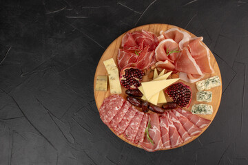Italian appetizers or antipasto set with gourmet food on black background, top view. Mixed delicatessen of cheese and meat snacks. Charcuterie board. Format of the banner.