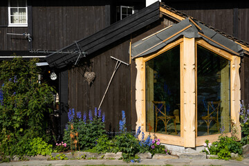 a dark wooden facade where there is an extension made of light wooden boards and glass, a rake and...