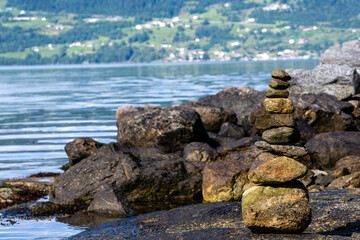 light brown and gray stones stacked on top of each other with the blue water of the fjord and the rocky coast in the background