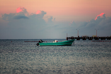 Naklejka premium Colorful sunrise at the magic hour of the day in the caribbean sea with a boat in the ocean water, beautiful colorful photo with a warm sky and clouds.
