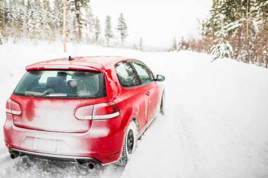 Rear view of red sports car driving on snowy road.