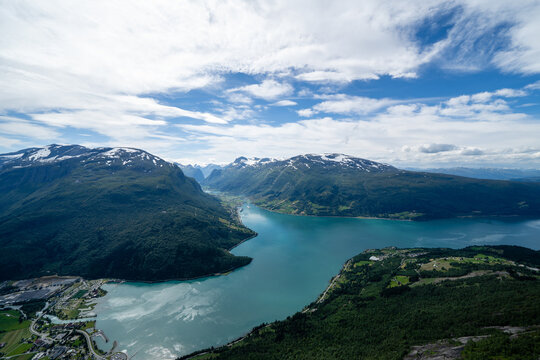 Norwegian mountain landscape from a high mountain down in the valley there is a village and in the distance between the mountain you can see a fjord with blue water above which there is beautiful sky © Rolands