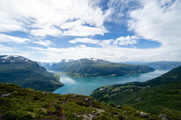 Norwegian mountain landscape from a high mountain down there is a fjord with blue-green water and above it is a bright blue sky with fabulous white fluffy clouds