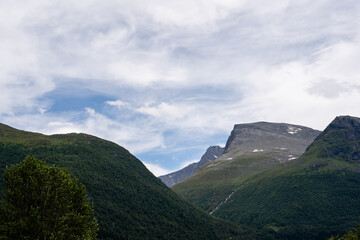 the dark mountains of Norway, covered with green moss, but above the rocky mountain tops is a blue sky with saturated white and gray clouds