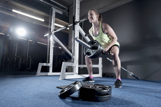 Young woman doing bent over row exercising with long barbell in the gym, Bavaria, Germany