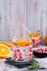 Hard seltzer alcoholic cocktail with orange, berries and rosemary in glasses on the table. Vertical view