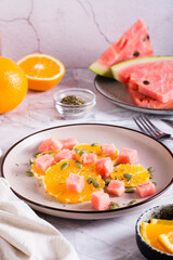 Fruit salad of watermelon, orange and pumpkin seeds on a plate on the table. Healthy food. Vertical