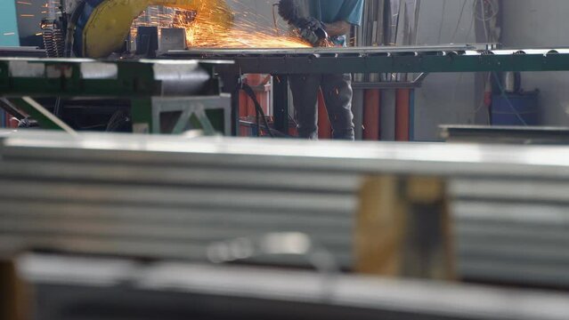 The interior of a heavy engineering plant with an industrial worker using an angular grinding machine and a cutting metal pipe