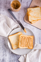 Bread toast with peanut butter on a plate and a jar of butter on the table. Top and vertical view