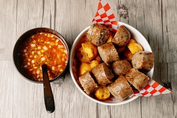 Top view of colombian morcilla blood sausage and a bowl of vegetable soup on a wooden table