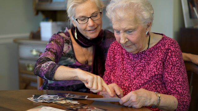 Senior elderly smiling woman looking at old photos and remembering memories with daughter at the dining room table.