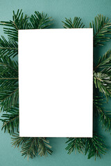 Christmas card mock up. Modern greeting card flat lay with green fir branches on green background. Empty postcard template with space for text. Merry Christmas and Happy Holidays!