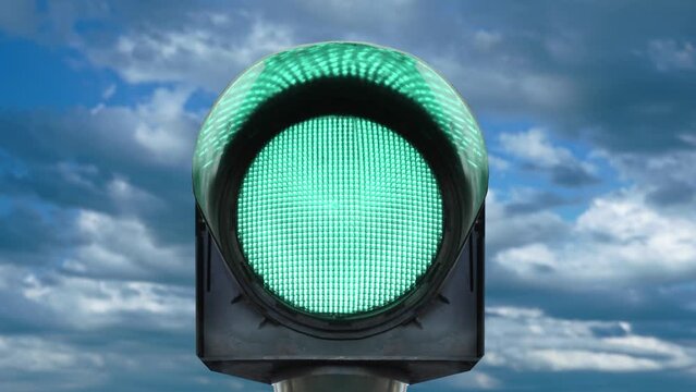 Single lamp semaphore on pole with lights changing colors on small screen against blue sky with heavy clouds combined shot closeup
