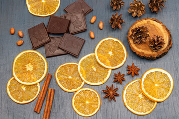Slices of dry orange, pieces of chocolate, cinnamon sticks and cones on a stump.