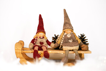 Christmas toys - two gnomes in christmas hats sitting on a sledge on white snowy background